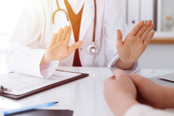 istock Unknown woman-doctor and patient discussing something while sitting at the table in sunny clinic, close-up 1254409344