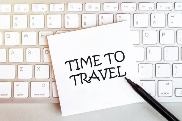 piece of paper with text TIME TO TRAVEL on the keyboard on a white background with a black felt-tip pen