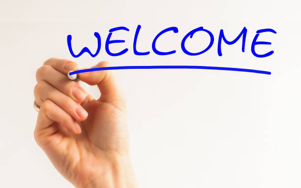 istock Welcome - Female hand with pen writing blu text on white background 1254411519