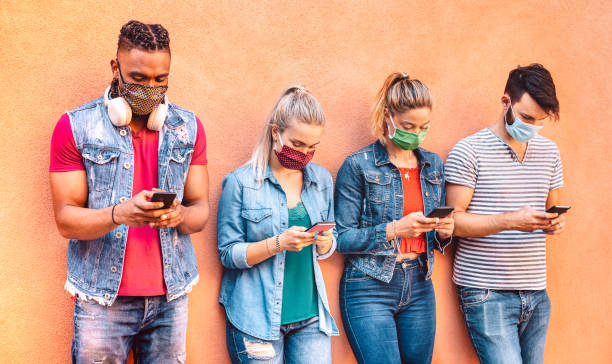 istock Multiracial friends with closed face masks using tracking app with mobile smartphones - Young milenial people sharing content on social media network - New normal lifestyle concept - Vivid filter 1254413214
