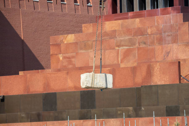 Crane lifts up concrete plate. Lenin's Mausoleum on Red Square in Moscow is visible in the background. Theme of repair and construction.