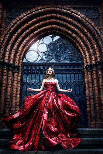 Fashion Model near Medieval Castle Gate Door, Woman Beauty Glamour Portrait in Elegant Waving Red sparkling Dress