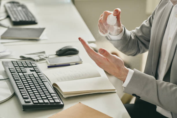 istock Young elegant businessman spraying santitizer on his hands while sitting by desk 1254416565
