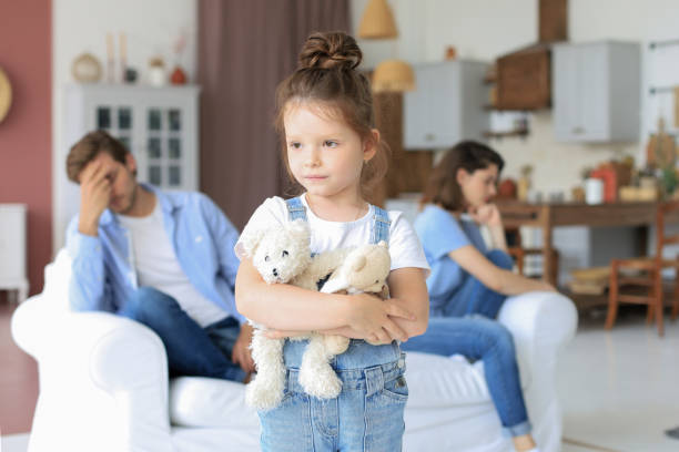 istock Young scolded parents sitting opposite each other on couch while little defenseless daughter upset looking at camera. 1254419735
