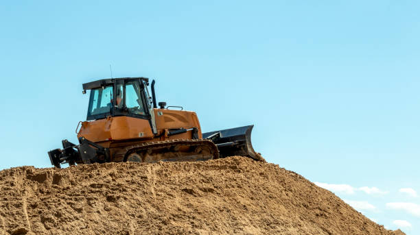 un bulldozer su una grande pila di sabbia contro un cielo blu - caterpillar truck foto e immagini stock