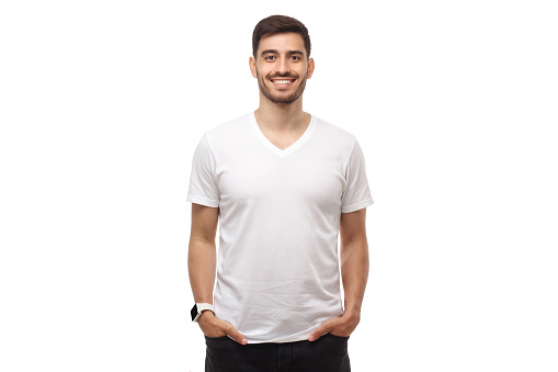 Front mockup of young man standing with hands in pockets, wearing blank white t shirt with copy space, isolated on studio background