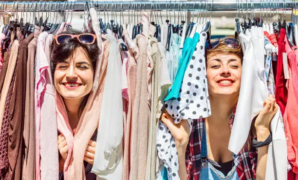Happy women at weekly flea market - Female friends having fun together shopping cloth on sunny day - Millenial lifestyle concept with girlfriends enjoying everyday life moments - Bright vivid filter