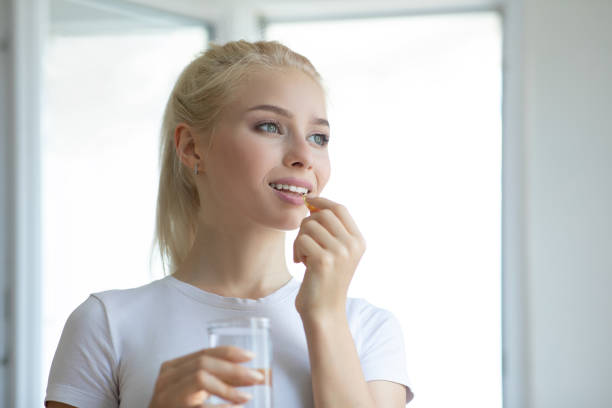 mujer tomando píldora con aceite de hígado de bacalao omega-3 - cod liver oil capsule vitamin pill vitamin e fotografías e imágenes de stock