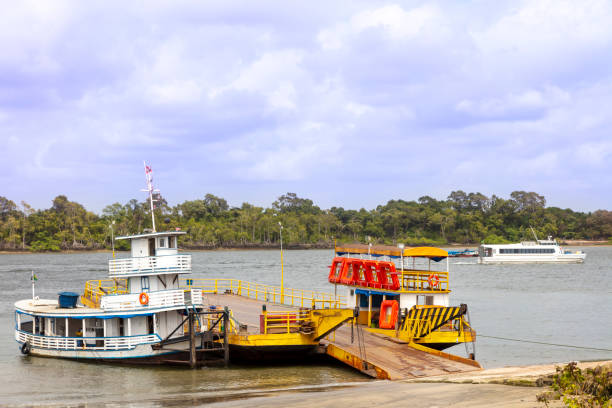 Catamaran sails carrying passengers (background).\nSoure route in Marajo Island. The ferry transports people, cars, trucks and motorcycles.