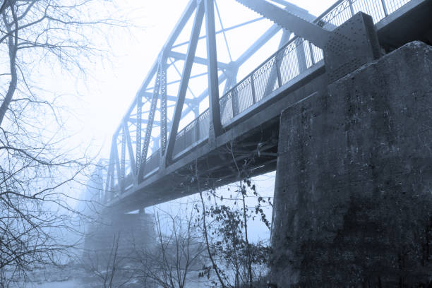 Looking down river at old railroad train truss bridge reflecting in foggy water