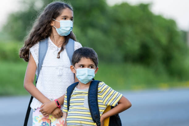 istock Hispanic siblings waiting for the bus while wearing protective face masks 1254432625