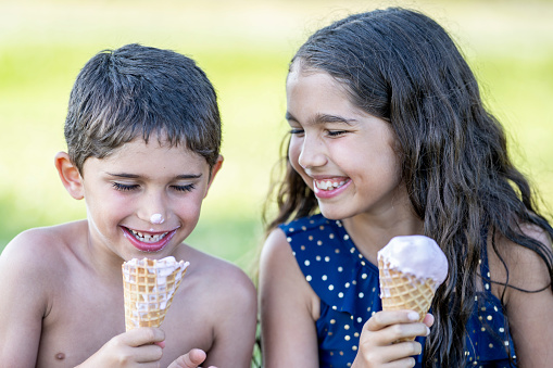 Cute brother and sister eating ice cream outside in the summer sun.