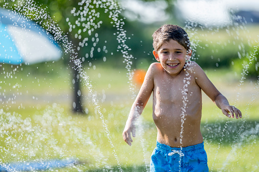 Young Latino boy running through a sprinkler in the heat of summer in the backyard
