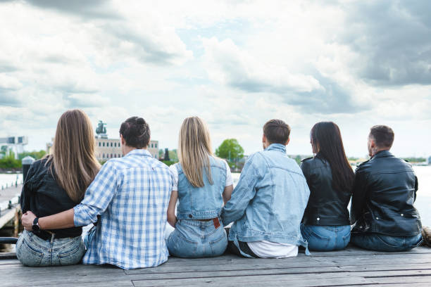 istock Group of people sitting on a pier beside a river 1254443940