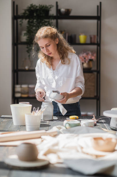 istock Female potter glazing raw unburned ceramic cup using brush. Earthenware mug putting colorant on pottery workshop 1254446813