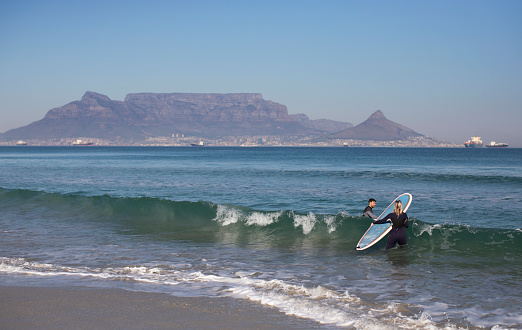 A young couple goes surfing during the Coronavirus pandemic on Blouberg beach in Cape Town South Africa.