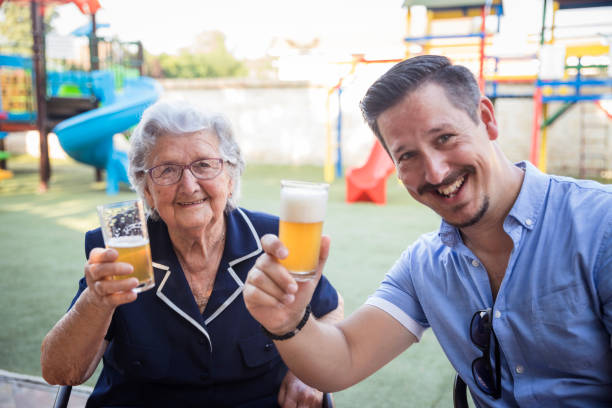 Happy young man drinking beer with his old mother for her birthday Joyful senior woman celebrating birthday with family 90 plus years photos stock pictures, royalty-free photos & images