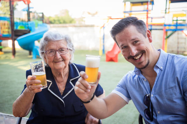 happy young man drinking beer with his old mother for her birthday - 96 well imagens e fotografias de stock