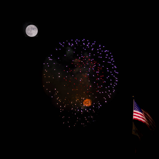 This photo was taken during a full moon and shows a firework display along with an American flag flying on a pole.  The shot was taken from a distance so that the moon, fireworks, and flag are all in focus and in frame.  Illumination levels of the moon and fireworks were seperately adjusted so that details of both are clear.