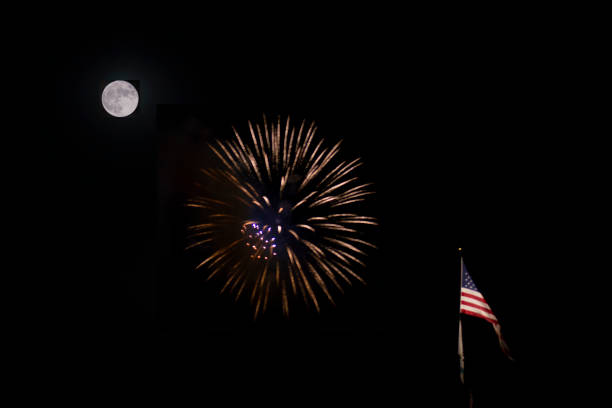 This photo was taken during a full moon and shows a firework display along with an American flag flying on a pole.  The shot was taken from a distance so that the moon, fireworks, and flag are all in focus and in frame.  Illumination levels of the moon and fireworks were seperately adjusted so that details of both are clear.