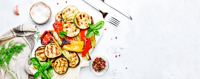 Grilled colorful vegetables, aubergines, zucchini, pepper with spice and green basil on serving board on white background. Panoramic banner with copy space
