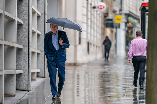 London is renowned for its rainy weather.  Virtually everybody carries and umbrella.  This image depicts a businessman walking along High Holborn in Central London during a rainy commute once the working day had ended.