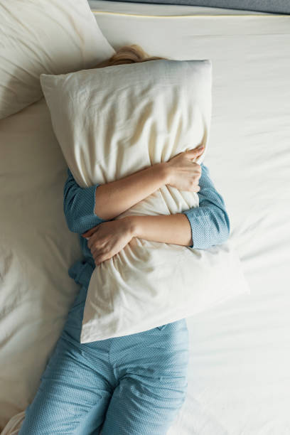 Unrecognizable Woman in Pyjamas Hugging a Pillow in Bed