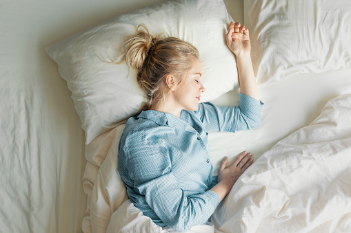 Pretty blonde woman in blue pyjamas sleeping peacefully in her bedroom, an overhead view.