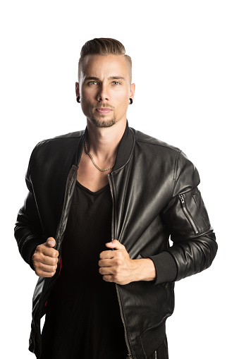 Attractive young bearded
man wearing a trendy black leather jacket and black shirt
looking angry at the camera with both hands holding
his jacket and standing against white background.