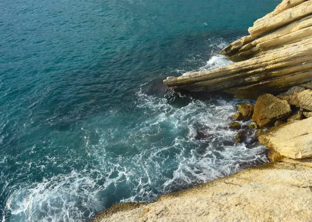 Mediterranean sea coast with sand-colored rock and backwash foaming wave.