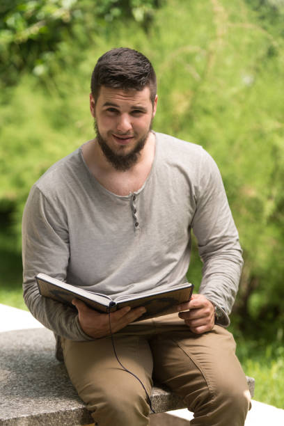 istock Young Muslim Guy Reading The Koran In Park 1254473828