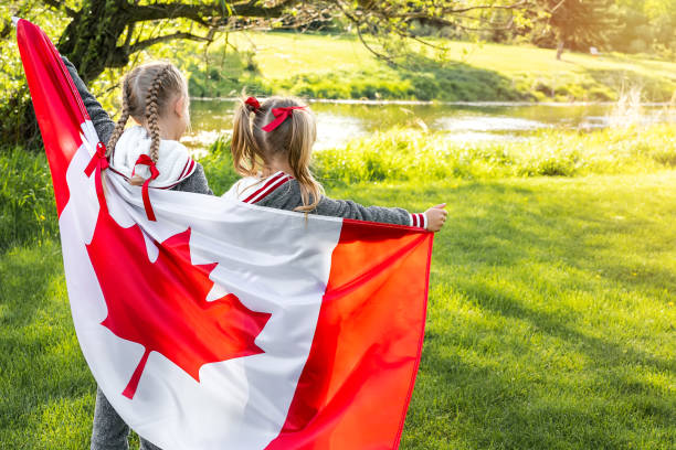 Happy Canda Day Celebrtation concept. Two cute female kids with Canadian flag. Back view Happy Canada Day Celebration. Two girls with braided hair are at nature background with big Canada flag in their hands. Young Canadian caucasian kids standing with back to the camera. 1st of July canada day photos stock pictures, royalty-free photos & images
