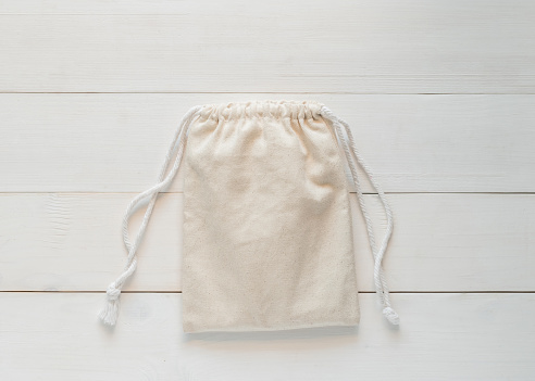 Canvas bag with drawstring, mockup of small eco sack made from natural cotton fabric cloth flat lay on white wood background from top view