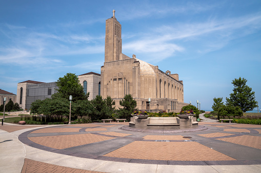 Panoramic image of the art deco Madonna della Strada Chapel on Loyola University campus on Lake Michigan with the sun in the blue sky above and beautiful masonry plaza below.