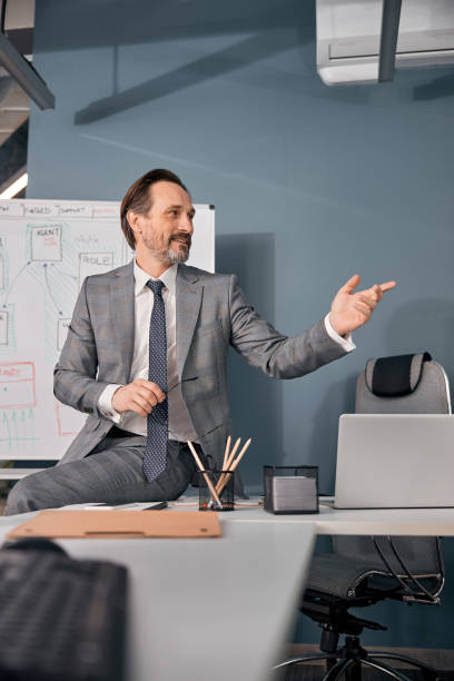 istock Handsome man sitting on table in office 1254478198