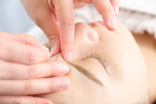 gros plan d’une femme et les mains de son praticien étant donné des aiguilles d’acupuncture sur son visage dans une clinique d’acupuncture. - acupuncturist photos et images de collection