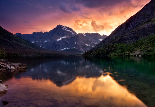 As raindrops still gently form their rings, the storm that had brought us rain that day finally cleared just as the sun set and the sky glowed in red and orange in response Lake Josephine in Glacier National Park, Montana