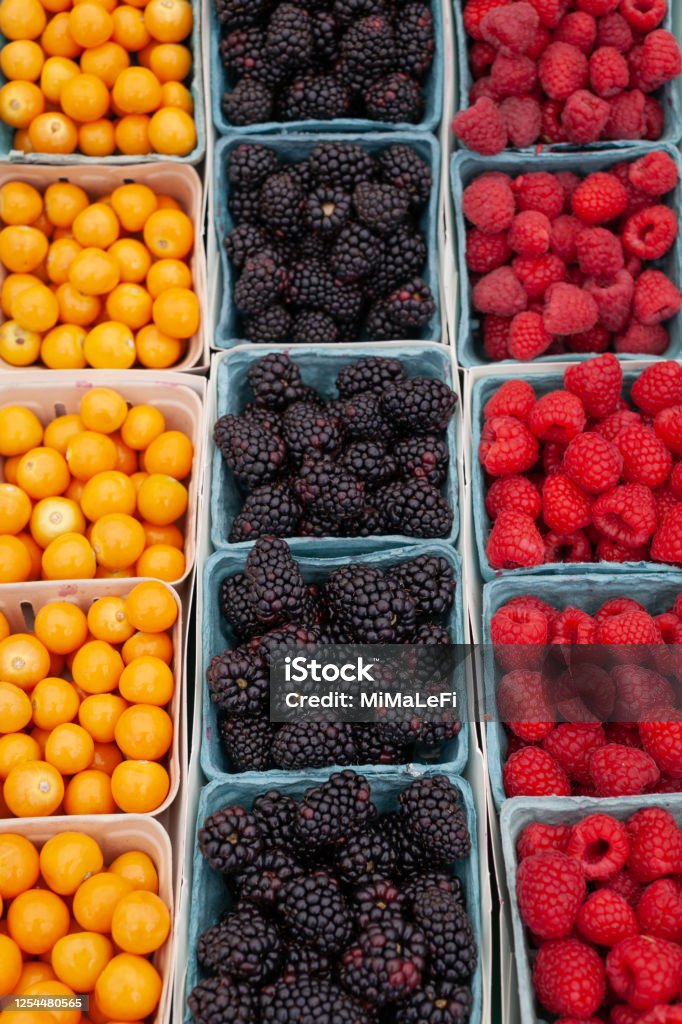 Organic fresh berries in a small blue carton boxes. Picking berry at American farm. Selling fresh juicy raspberries, blackberries, physalis, blueberries at the farmers market. Healthy food concept. Puzzle Stock Photo