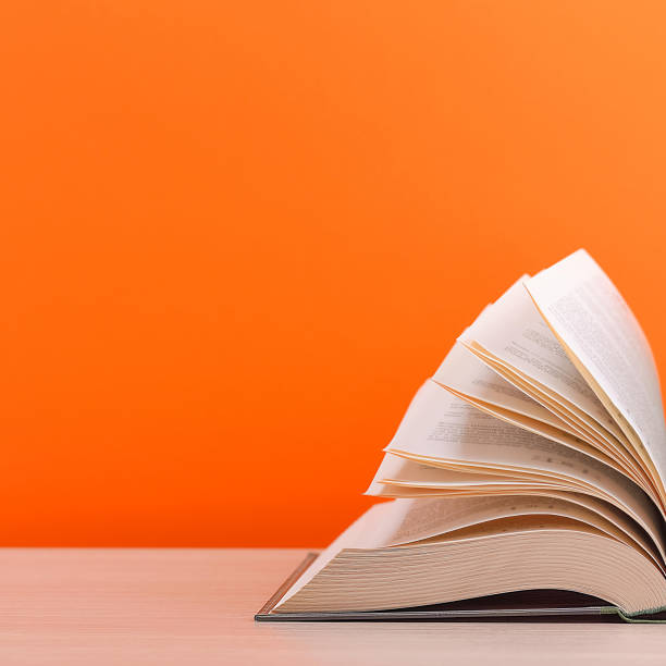 istock The book is open, lying on the table, sheets fanned out on a orange background. 1254489127
