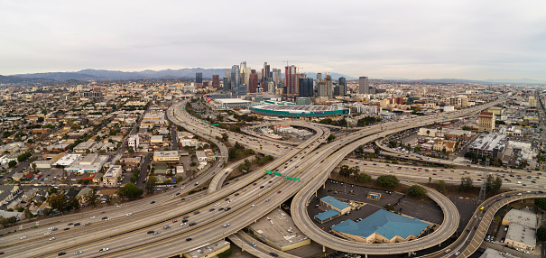 The remote scenic aerial view of Downtown Los Angeles from West Washington Boulevard, over the huge overpass crossing between Santa Monica Freeway and Harbor Freeway and Transit Way. California, USA. The cloudy afternoon of the autumn day. 4K UHD drone video footage with the backward camera motion.