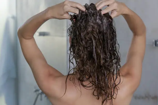 Photo of Hair shampooing and scalp massage. Back view of woman in the shower cabin.