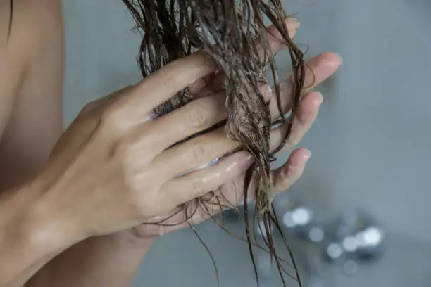 Photo of Woman applaying conditioner on her wet tangled hair in the shower cabin.