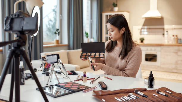 istock Wake up and Make up. Young female blogger applying makeup, testing cosmetic products while recording a tutorial video for her beauty blog using camera at home 1254496232