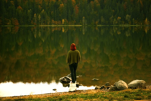 Rear view of redhead woman standing on the edge of lake, looking and admiring the view