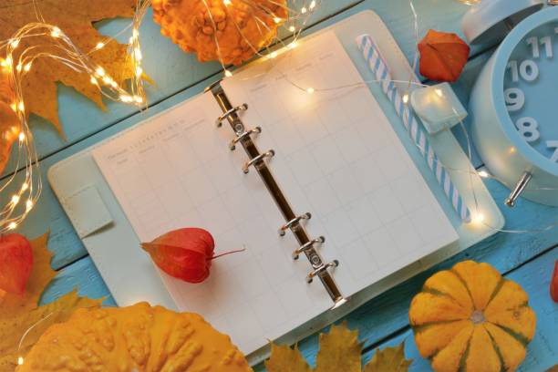 istock Back to school. Lesson plan.Studying time.Timetable of classes. Blank notepad,pumpkins and yellow maple leaves, headphones, shining garland and alarm clock on a blue background. 1254502181