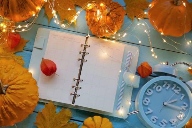 istock Back to school. Lesson plan.Studying time.Timetable of classes. Blank notepad,pumpkins and yellow leaves, headphones, shining garland and a blue alarm clock on a blue background. 1254502200