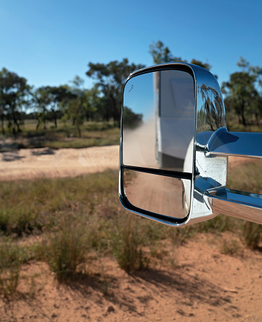 Car side mirror reflecting a blurred vision of a caravan traveling on a dirt road in the Australian outback