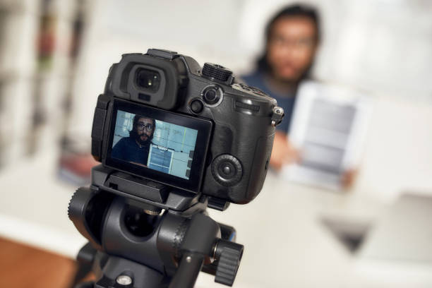 istock Young man teaching online, looking at camera and explaining new theme while working from home. Focus on camera, professional digital equipment 1254505605