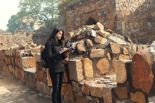 Indian college female student collecting information in the old fort and making college project. summer vacations work. outdoor shoot. location is Delhi old fort.