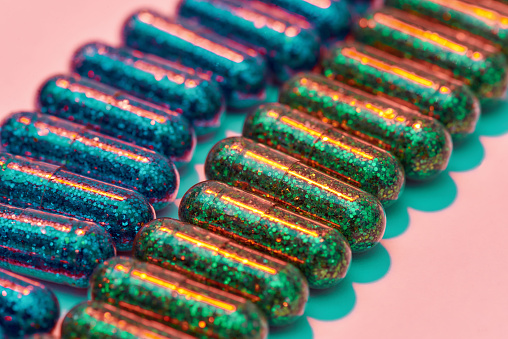 Creative concept with many green and blue glitter pills lying in two rows isolated on pastel pink background. Minimal style, art concept. Horizontal shot. Selective focus